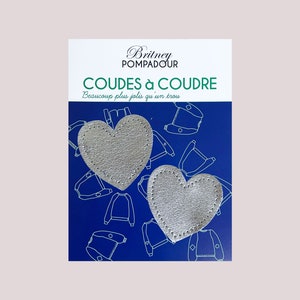 Peut inclure: Deux empiècements de coude en forme de cœur argentés sur un fond bleu avec le texte "Britney Pompadour Coudes à Coude Beaucoup plus jolis qu'un trou".