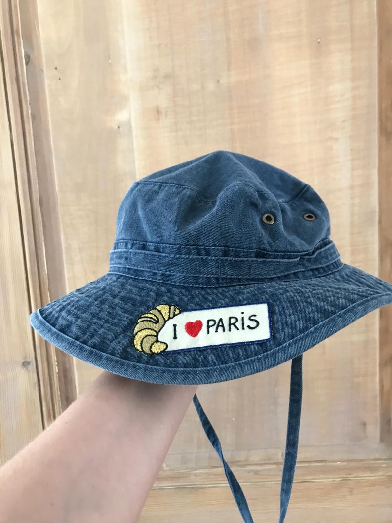 May include: A blue denim bucket hat with a patch that says "I love Paris" and a yellow croissant graphic.