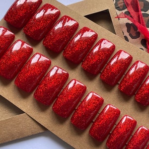 May include: A set of ten red glitter press-on nails. The nails are arranged in two rows of five on a brown card.