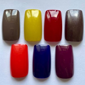 May include: Seven rectangular nail polish samples in various colors: brown, yellow, red, bronze, red, blue, and purple. The samples are arranged in two rows, with four on top and three below.