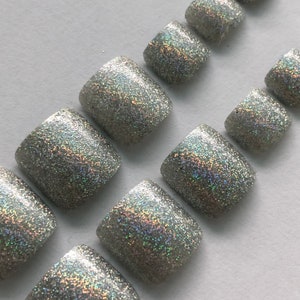 Puede incluir: Conjunto de diez puntas de uñas de los pies de purpurina plateada. Las puntas son de forma cuadrada y tienen un acabado holográfico.