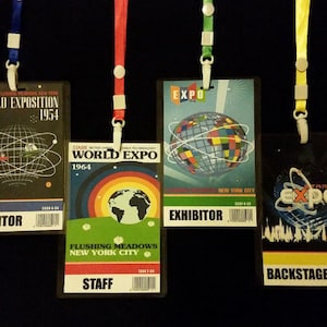 May include: Four vintage Stark World Expo badges from 1954, 1964, and 1974, with lanyards. The badges are for Visitor, Staff, Exhibitor, and Backstage. Each badge features unique graphics and text, including the Expo logo and location.