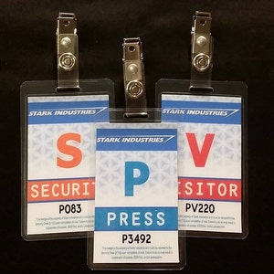May include: Three clear plastic ID badge holders with metal clips. The badges are for Stark Industries and have different colored letters and text. The first badge says "Security" with the number "P083". The second badge says "Press" with the number "P3492". The third badge says "Visitor" with the number "PV220".