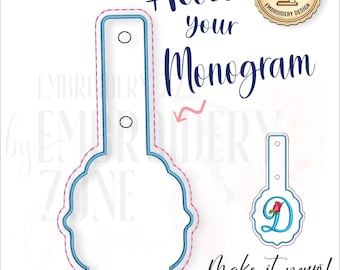 Puede incluir: Un archivo de diseño de bordado con forma de etiqueta de bordes festoneados y una lengüeta vertical con dos orificios circulares. El diseño incluye contornos de costura azules y rosas. El texto dice Add your Monogram y Make it yours.