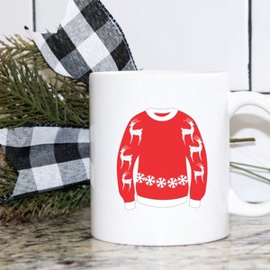 May include: White ceramic coffee mug with a red and white Christmas sweater design featuring reindeer and snowflakes. The mug has a handle on the right side.