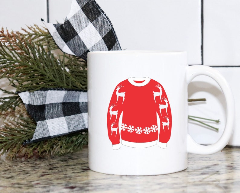 May include: White ceramic coffee mug with a red and white Christmas sweater design featuring reindeer and snowflakes. The mug has a handle on the right side.