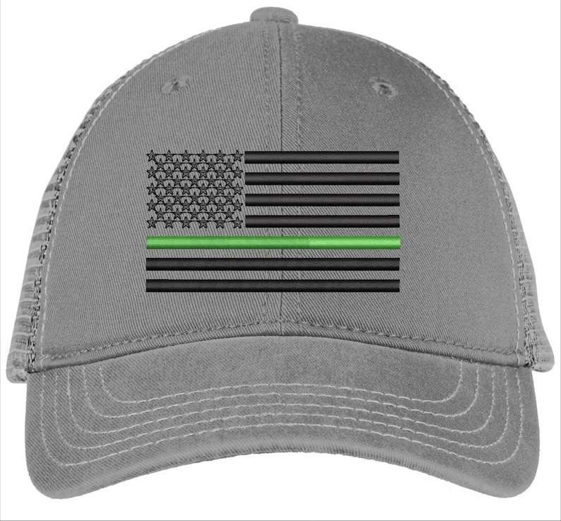 Op de afbeelding: Een grijze truckercap met een Amerikaans vlagontwerp in zwart en groen. De vlag heeft een dunne groene streep in het midden, die de dunne groene lijn voorstelt.