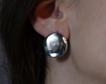 May include: A pair of silver round earrings with a slightly textured surface.