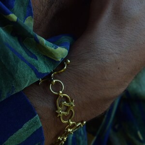 Puede incluir: Un brazalete de cadena dorada con un dise&ntilde;o decorativo. El brazalete se lleva en la mu&ntilde;eca.