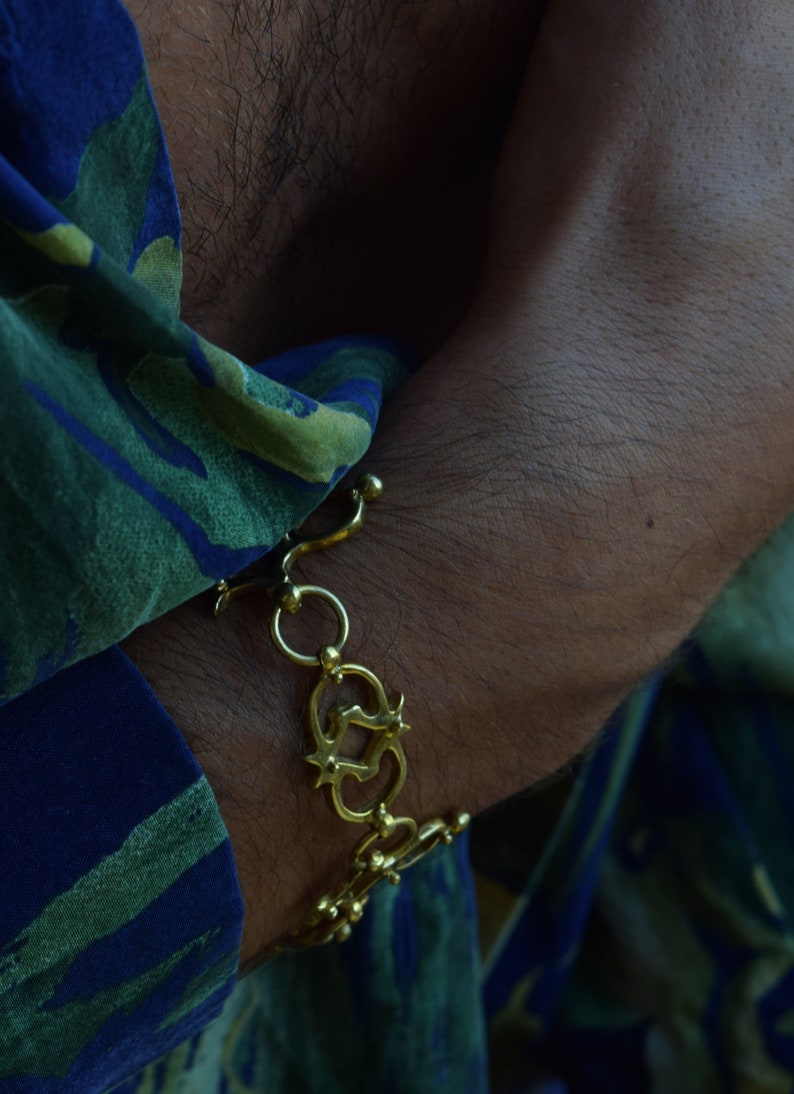 Puede incluir: Un brazalete de cadena dorada con un dise&ntilde;o decorativo. El brazalete se lleva en la mu&ntilde;eca.