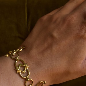 Puede incluir: Un brazalete dorado con un dise&ntilde;o &uacute;nico e intrincado que presenta c&iacute;rculos entrelazados y elementos en forma de estrella.