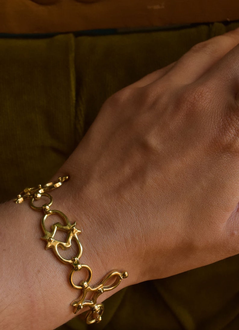 Puede incluir: Un brazalete dorado con un dise&ntilde;o &uacute;nico e intrincado que presenta c&iacute;rculos entrelazados y elementos en forma de estrella.