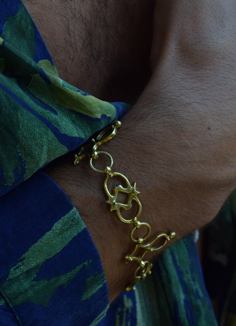Puede incluir: Un brazalete de cadena de oro con un dise&ntilde;o decorativo y adornado. El brazalete se lleva en la mu&ntilde;eca.