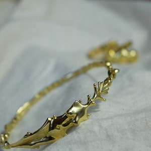 May include: A gold-toned bangle bracelet with a unique, organic design. The bracelet is made of twisted metal and features a large, abstract shape that resembles a branch or a piece of coral.