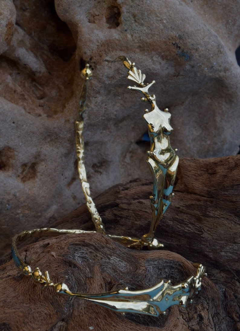 May include: Two gold-toned metal bracelets with a unique, abstract design. One bracelet features a stylized human figure.