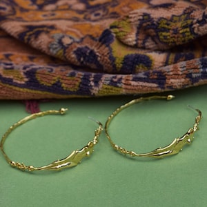 May include: A pair of gold hoop earrings with a unique, abstract design. The earrings are made of a thick, textured metal and have a slightly irregular shape.