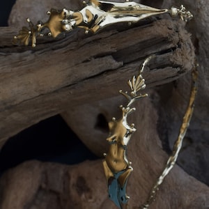 May include: A gold-toned metal bracelet with a unique design featuring a stylized human figure. The bracelet is crafted with a textured, organic-looking surface.