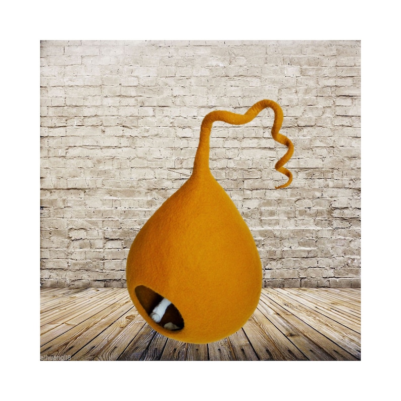May include: A bright orange felt cat bed shaped like a teardrop with a long, curled felt tail. The bed has a round opening for the cat to enter.