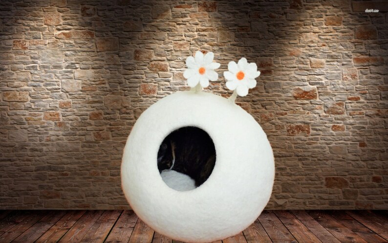 May include: White felt cat bed shaped like a sphere with two white felt flowers on top. The bed has a round opening for the cat to enter.