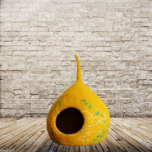 Könnte beinhalten: Ein gelbes Filzkatzenbett in Tropfenform mit einer kleinen Öffnung zum Betreten. Das Bett hat ein hellgrünes und weißes Design.