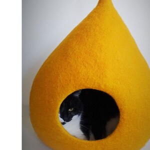 May include: A yellow felt cat bed shaped like a teardrop with a black and white cat inside.