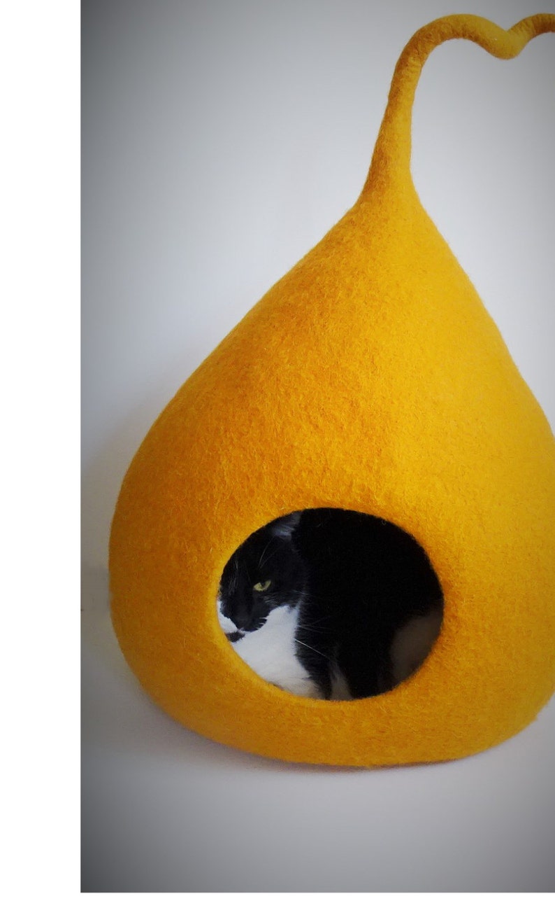 May include: A yellow felt cat bed shaped like a teardrop with a black and white cat inside.