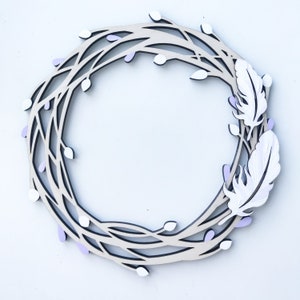 May include: A wooden wreath with a delicate, intricate design featuring branches and small purple flowers. Two white feathers are attached to the wreath, adding a touch of whimsy.