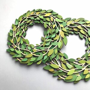May include: Two green paper wreaths made of layered leaves, with a light brown background.
