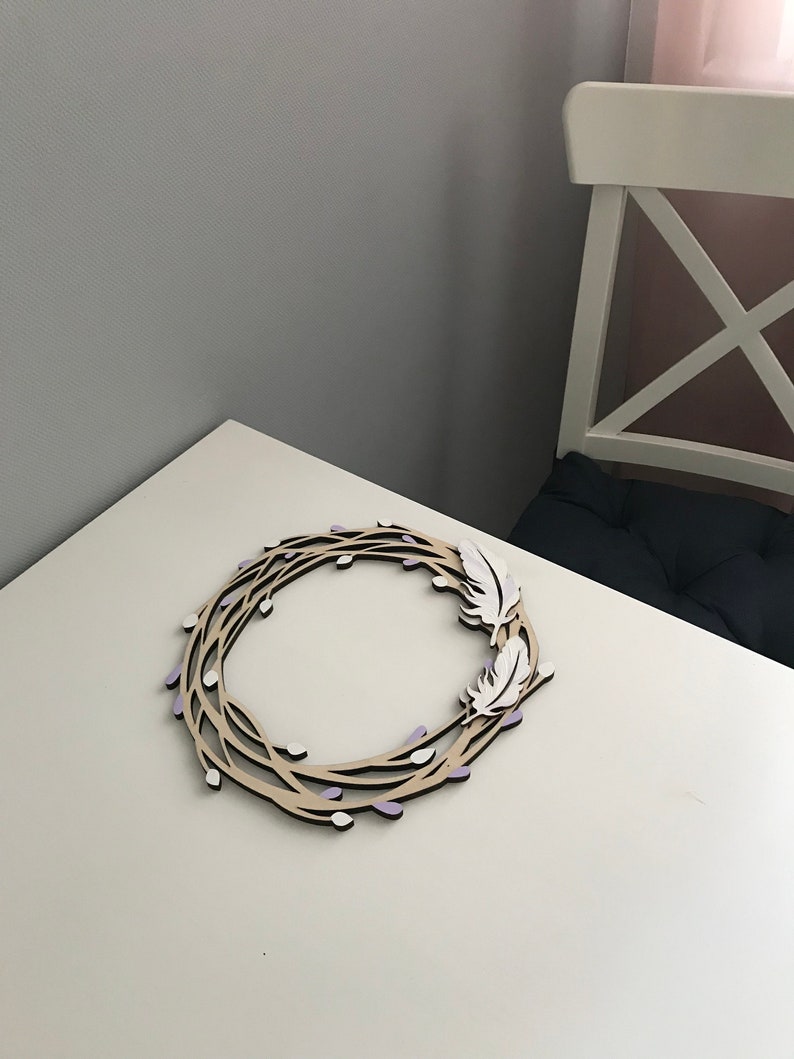 May include: A wooden wreath with a natural brown finish, decorated with white feathers and purple accents. The wreath is made of branches with small buds.