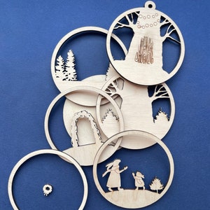 May include: Six wooden ornaments with various winter-themed designs, including a tree, a wreath, an archway, and a pair of rabbits. The ornaments are all cut out of wood and have a natural finish.
