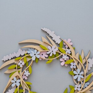 Puede incluir: Una corona de madera con un dise&ntilde;o floral. La corona est&aacute; hecha de madera marr&oacute;n claro y presenta flores rosas, azules y verdes.