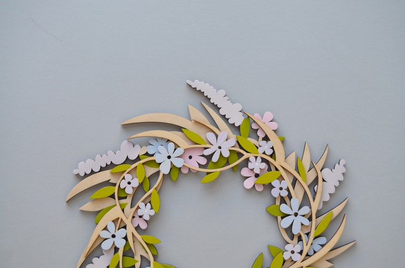 Puede incluir: Una corona de madera con un dise&ntilde;o floral. La corona est&aacute; hecha de madera marr&oacute;n claro y presenta flores rosas, azules y verdes.