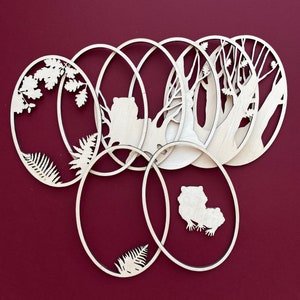 May include: Set of six wooden oval ornaments with various nature-themed cutouts, including trees, ferns, and animals. The ornaments are arranged in a circular pattern, with the cutouts facing outward.