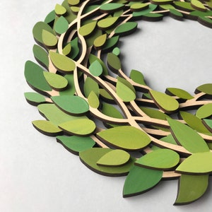May include: A green wreath made of layered wood leaves. The leaves are painted in shades of green and brown.