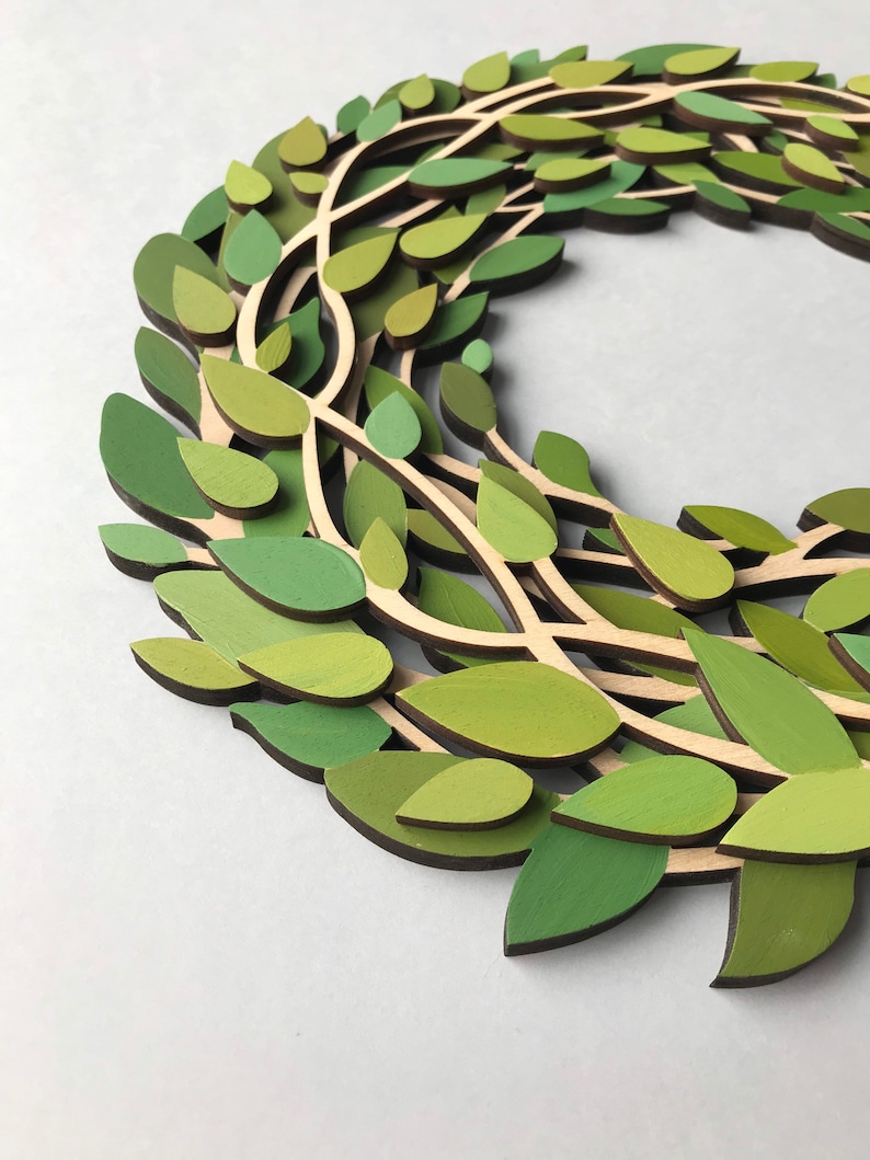 May include: A green wreath made of layered wood leaves. The leaves are painted in shades of green and brown.