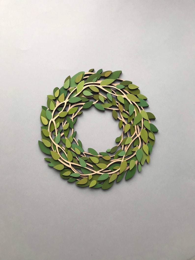 May include: A green paper wreath made of leaves and branches. The wreath is a circle and is made of paper that has been cut and layered to create a 3D effect.