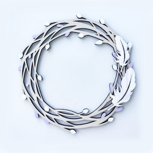 May include: A wooden wreath with a delicate, intricate design featuring branches and small white and purple flowers. Two white feathers are attached to the wreath, adding a touch of whimsy.