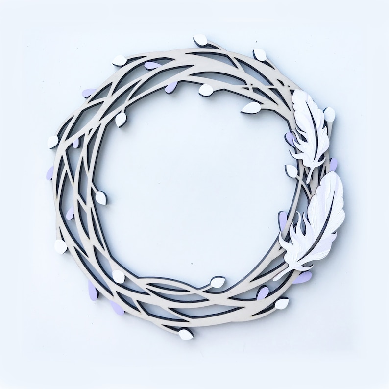 May include: A wooden wreath with a delicate, intricate design featuring branches and small white and purple flowers. Two white feathers are attached to the wreath, adding a touch of whimsy.