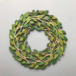 May include: A green paper wreath made of leaves and branches. The wreath is a circle and is made of paper that has been cut and layered to create a 3D effect.