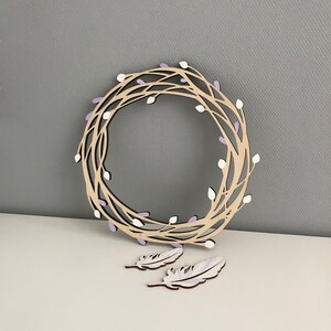 May include: A wooden wreath with a delicate design of branches and purple buds. Two white feathers are included.