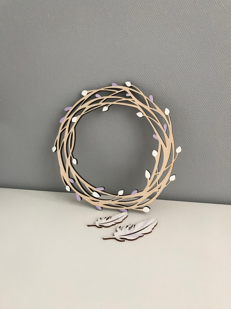 May include: A wooden wreath with a delicate design of branches and purple buds. Two white feathers are included.