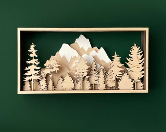 May include: A wooden wall decor featuring a 3D mountain range with a snowy peak and a forest of trees. The mountains and trees are cut out of wood and mounted on a wooden frame.