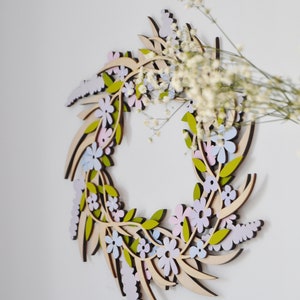 Puede incluir: Una corona de madera con un dise&ntilde;o floral. La corona est&aacute; hecha de madera marr&oacute;n claro y presenta delicadas flores en tonos de rosa, azul y verde.