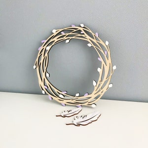 May include: A wooden wreath with a light purple and white floral design. Two white wooden feathers are included.