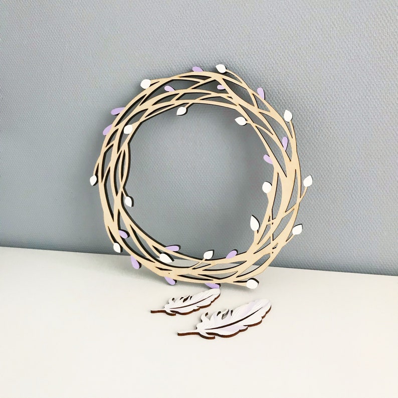 May include: A wooden wreath with a light purple and white floral design. Two white wooden feathers are included.