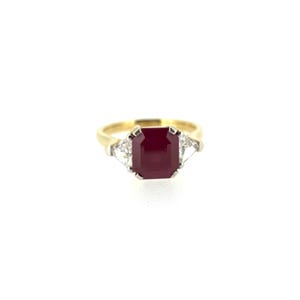 May include: A gold ring featuring a large, rectangular, deep red gemstone as the centerpiece. Two smaller, triangular, clear gemstones flank the main stone. The ring has a classic design, suitable for various occasions.