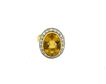 Pode incluir: Um anel de ouro com uma grande pedra de topázio ovalada cercada por um halo de diamantes menores.
