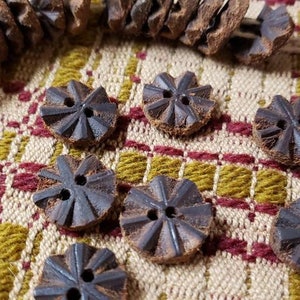 May include: A close-up of a collection of brown wooden buttons with a starburst design. The buttons are arranged on a checkered fabric background.