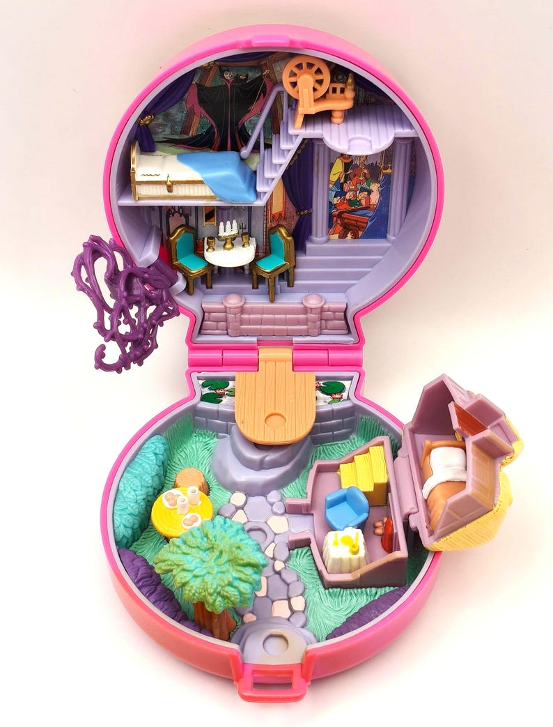 May include: A vintage pink and purple miniature playset, designed as a castle with various rooms and accessories. The playset includes a bed, table, chairs, and a garden area. The interior has a painted backdrop of a castle scene.