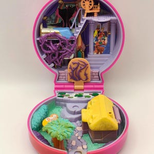 May include: A vintage pink and purple miniature playset, with a detailed interior including a bed, stairs, and a spinning wheel. The exterior features a yellow building, a small garden, and a stone path. The playset is open, revealing colourful illustrations.